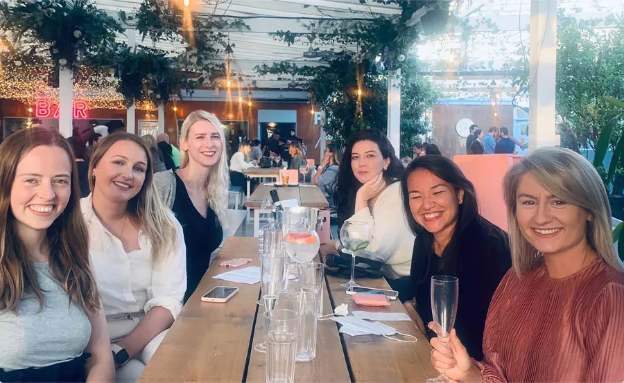 Six women around dinner table smiling at the camera.